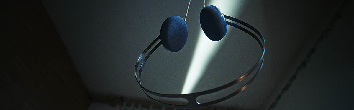 Blue AIAIAI Tracks Oklou Edition on-ear headphones suspended in a beam of light against a dark background.